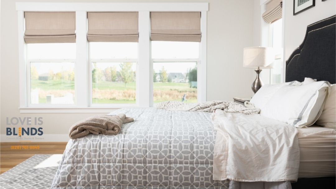 Bright bedroom with a bed, white bedding, gray patterned throw, and three window shades above the headboard