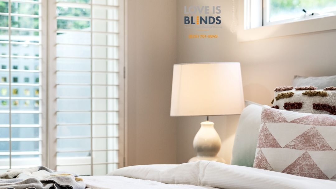 Bright bedroom with a lit white lamp, striped pillows, and white shutters by a window