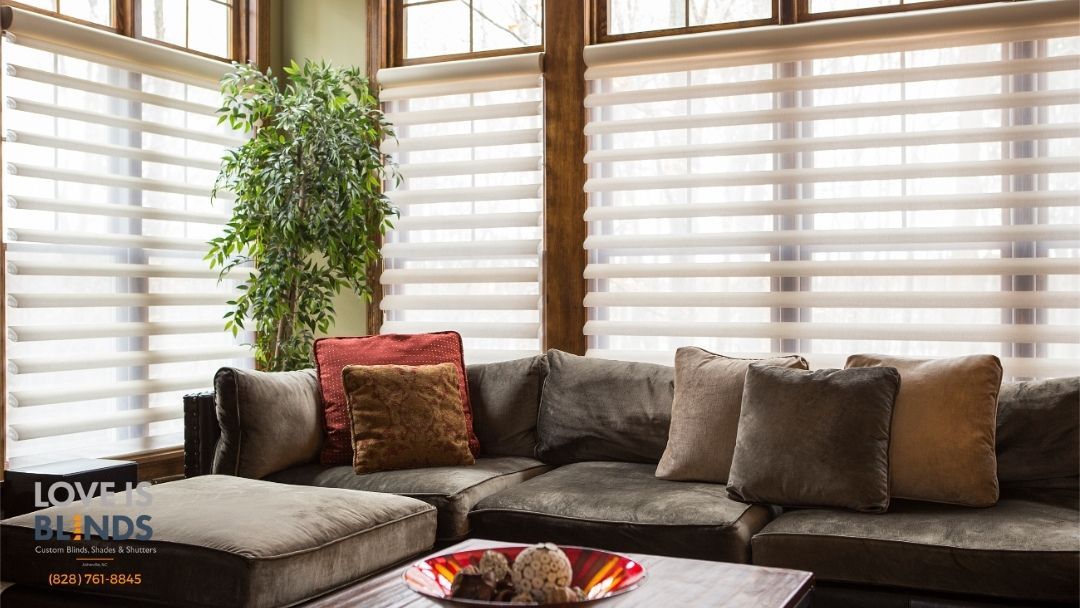 Bright living room with a large sectional sofa, pillows, potted plant, and window blinds.
