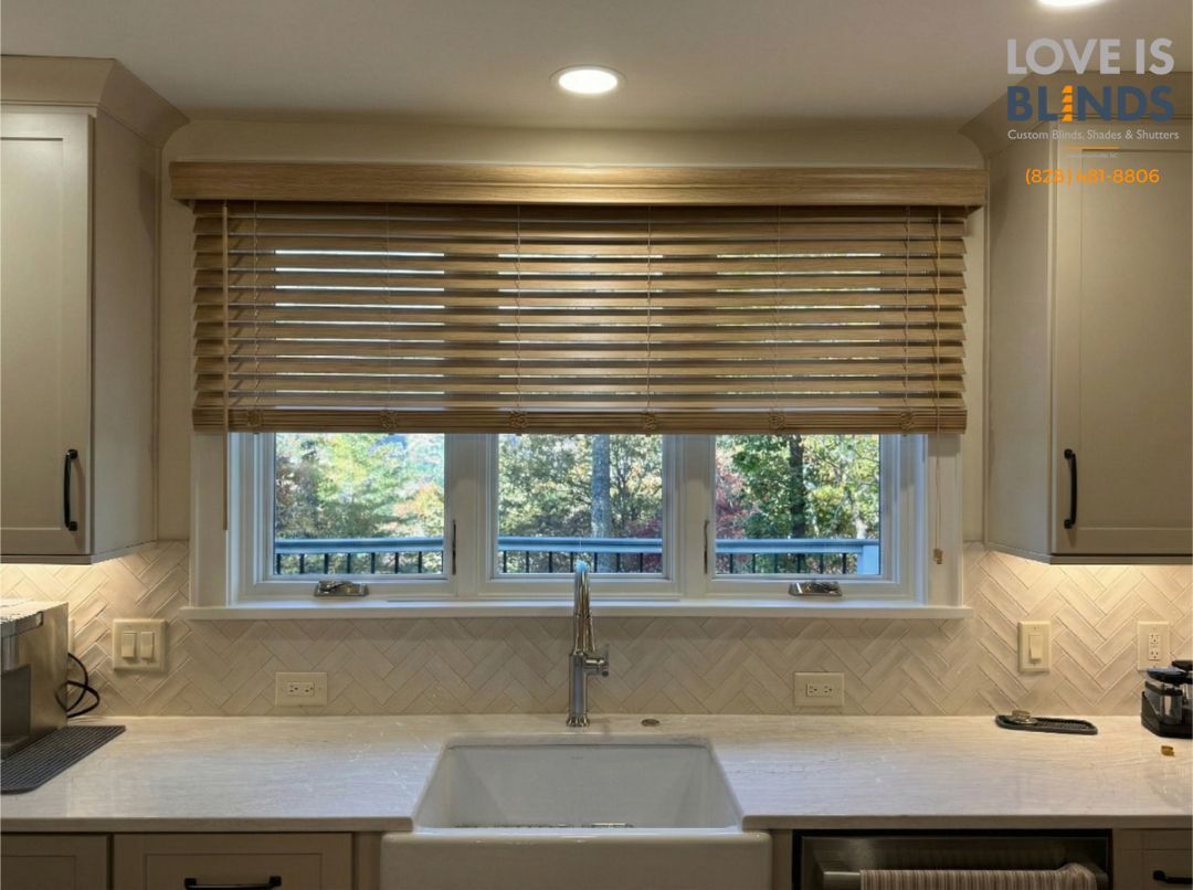 Bright kitchen sink beneath a window with wood blinds and light-colored cabinets
