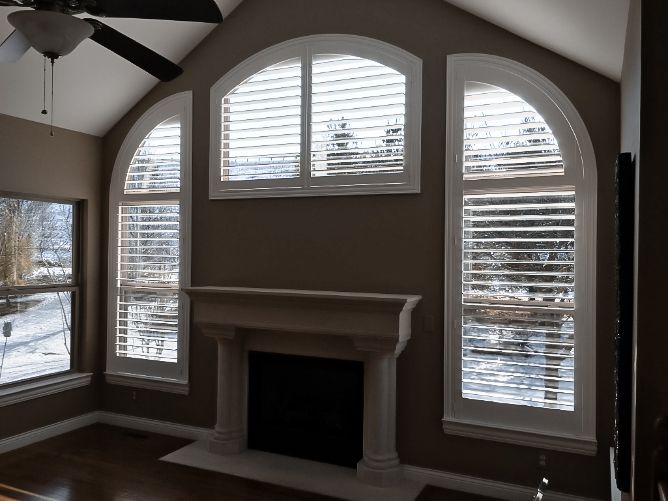 Living room with arched windows, white shutters, and a fireplace under a vaulted ceiling