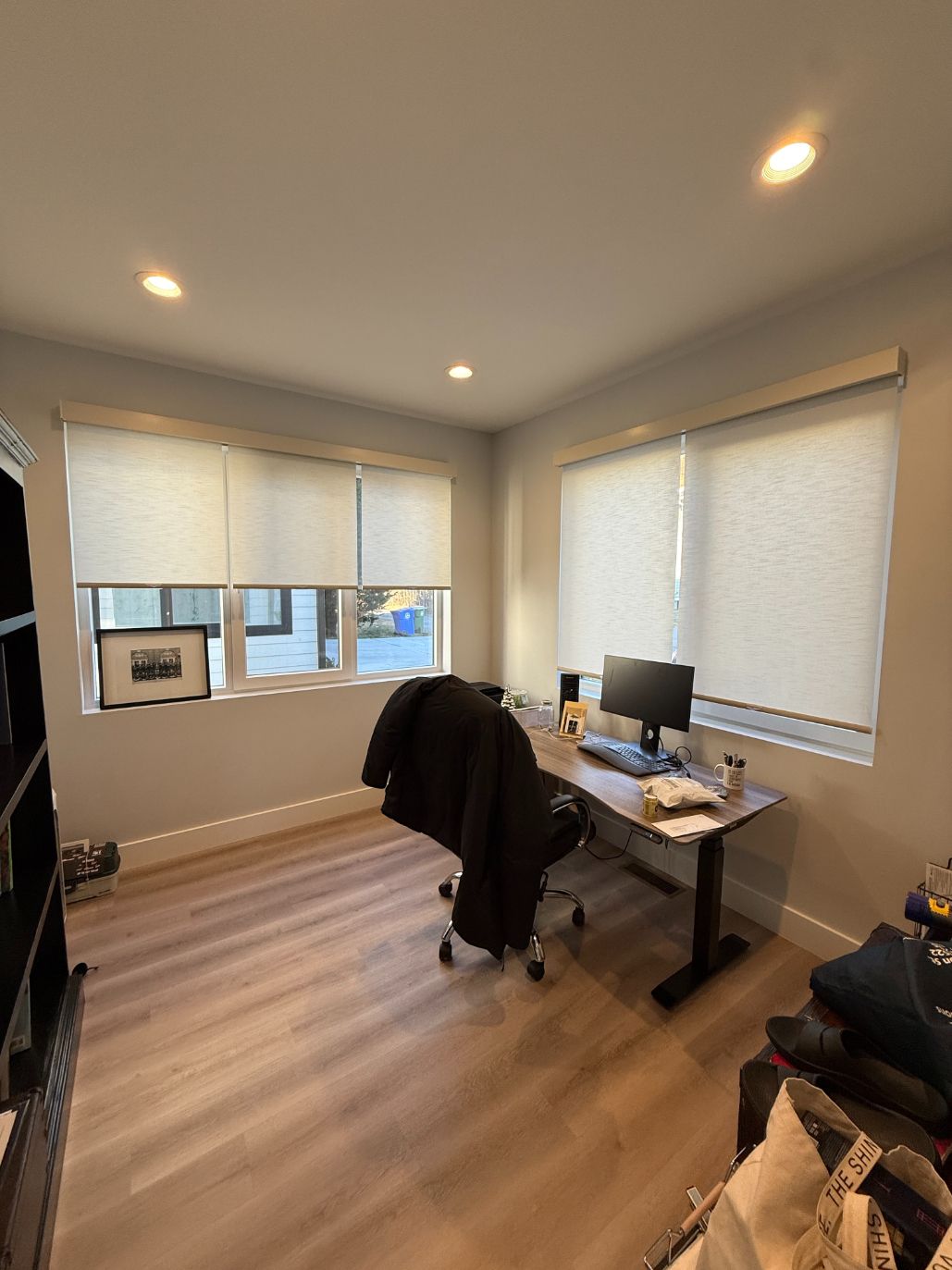 Home office with desk, computer, swivel chair, and large windows with blinds.
