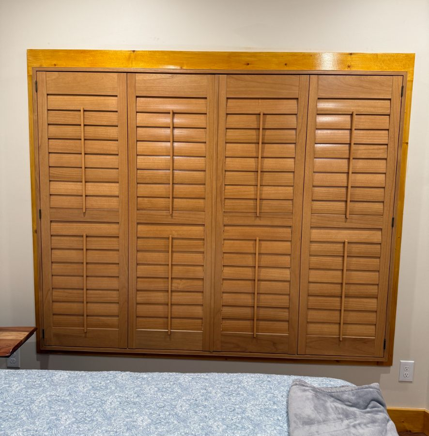 Wooden louvered closet doors on a beige wall above light blue carpet.