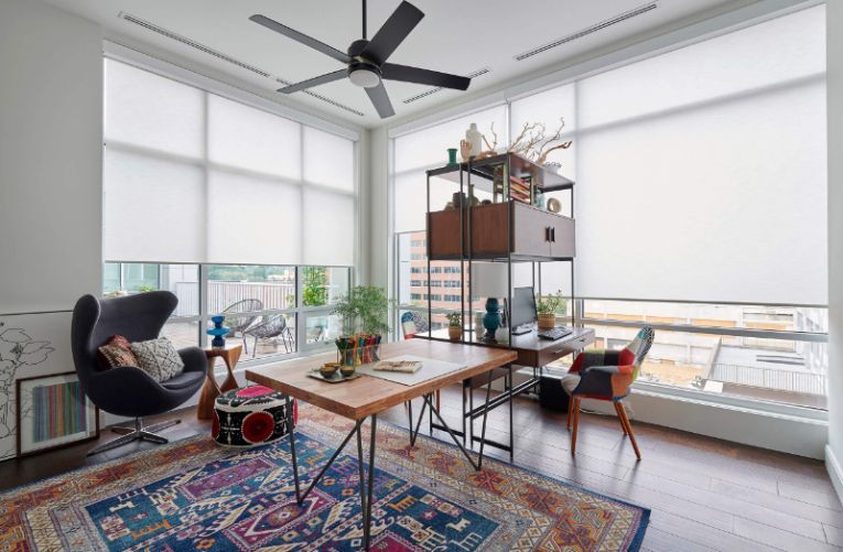 Bright modern living room with large windows, a table, chairs, shelving, and a patterned rug