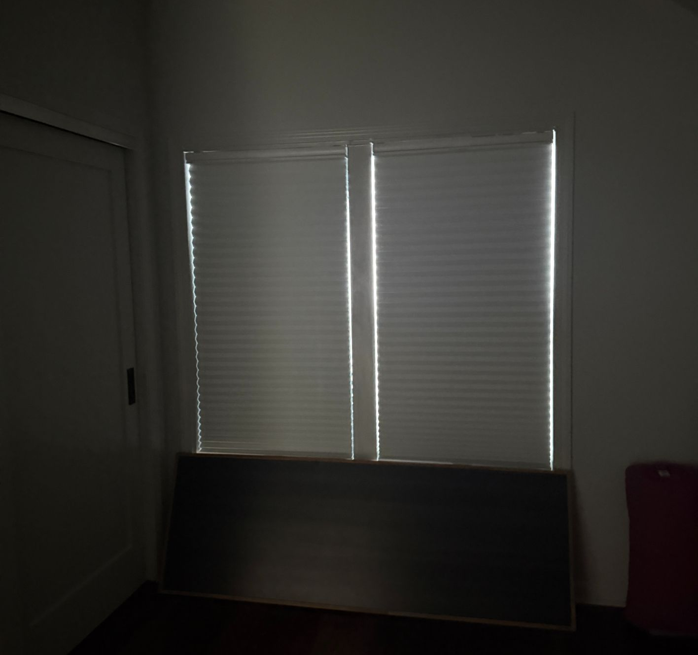 Dim room with closed white blinds and a board leaning against the window.