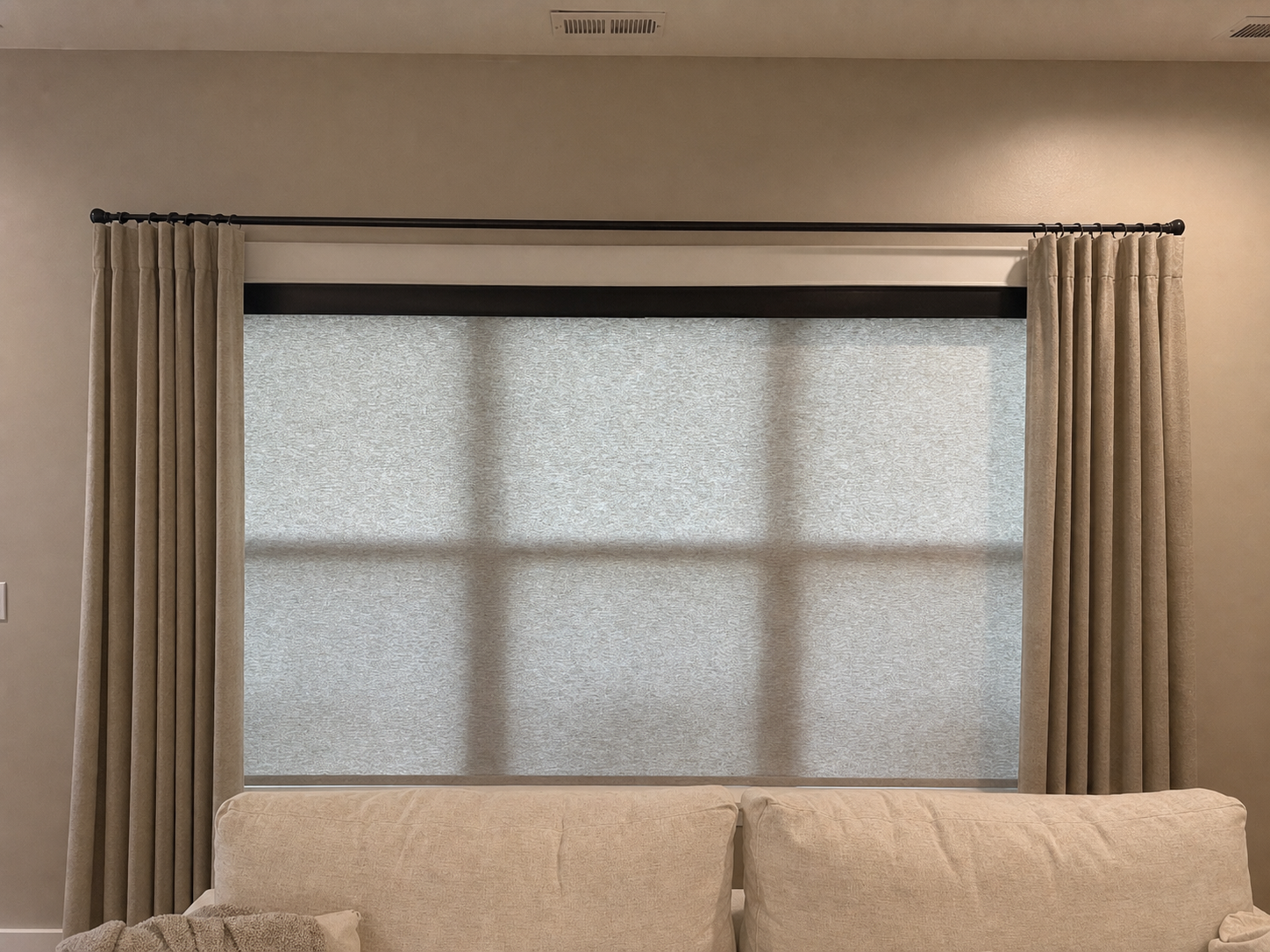 Living room window with gray curtains and roller shades above a beige couch