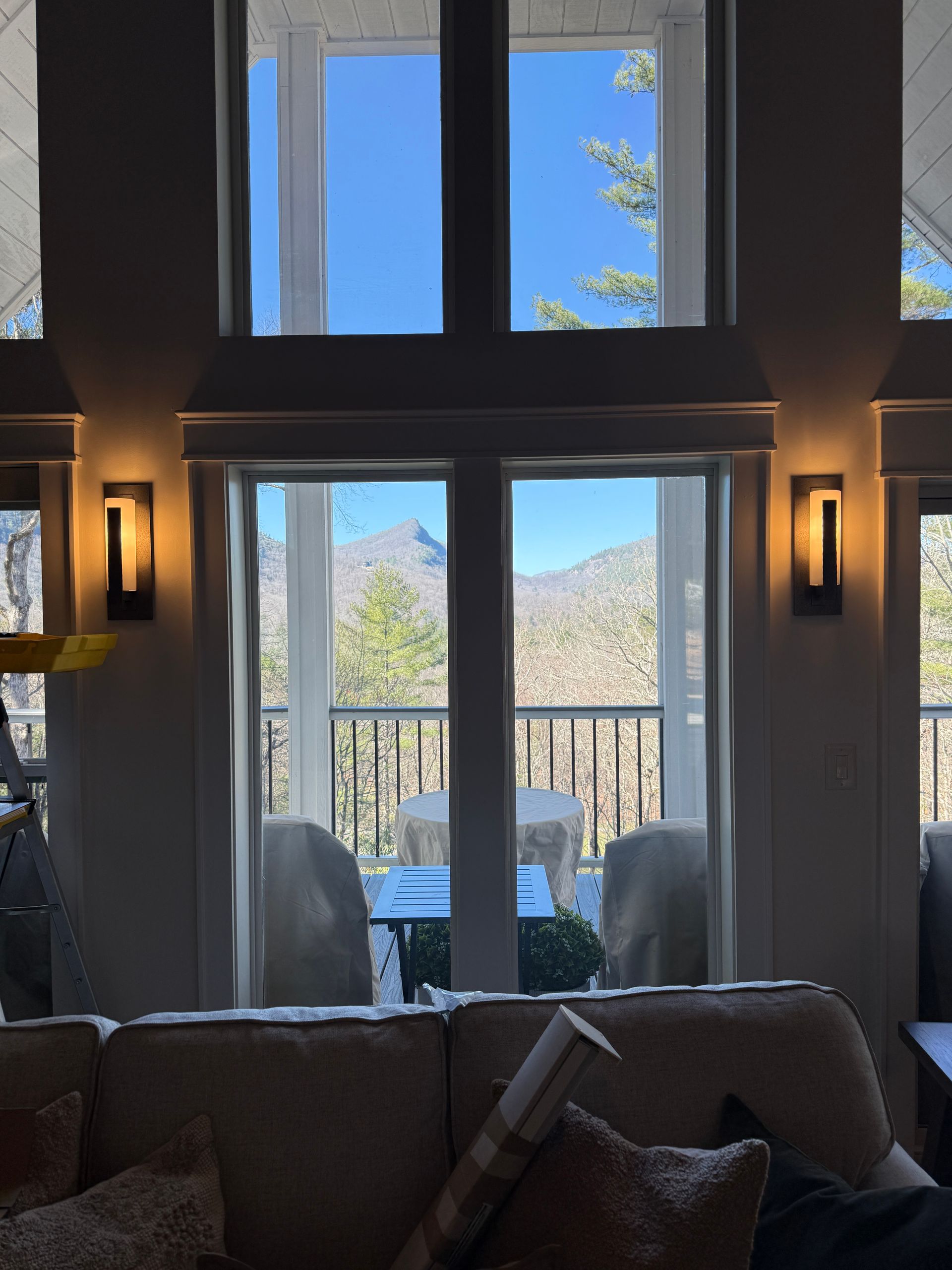 Cozy living room with tall windows, wall sconces, and a mountain view through a glass door.