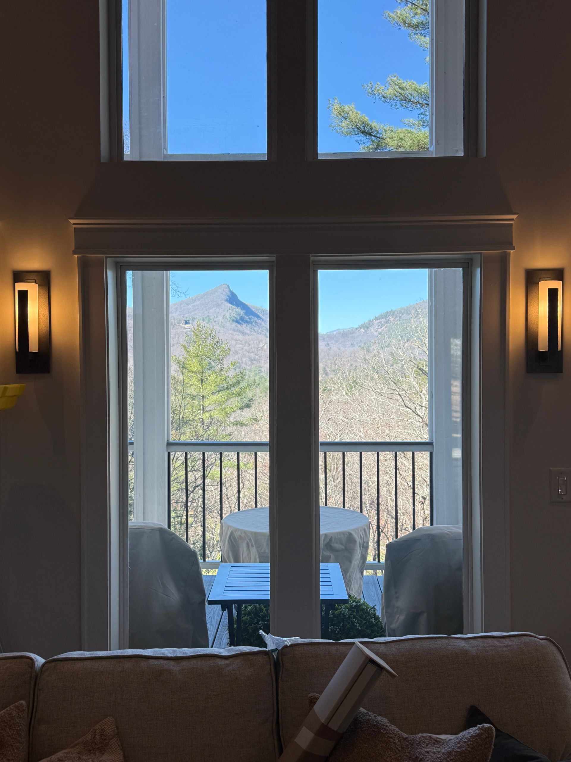 Living room view through tall windows to a balcony and mountain landscape beyond.