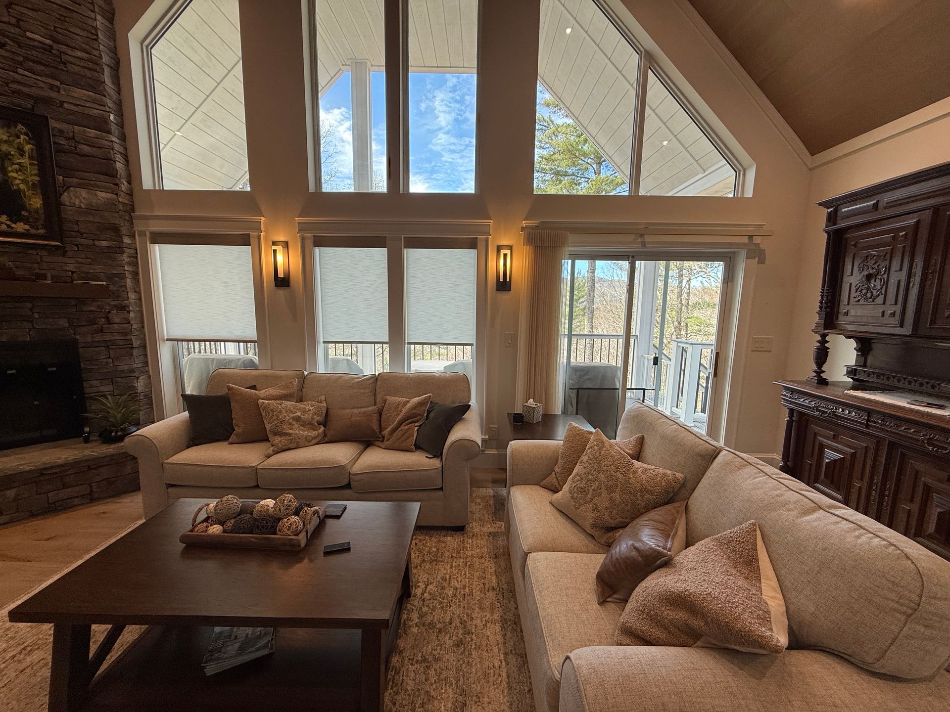 Spacious living room with high windows, beige sofas, a coffee table, and stone fireplace in warm light