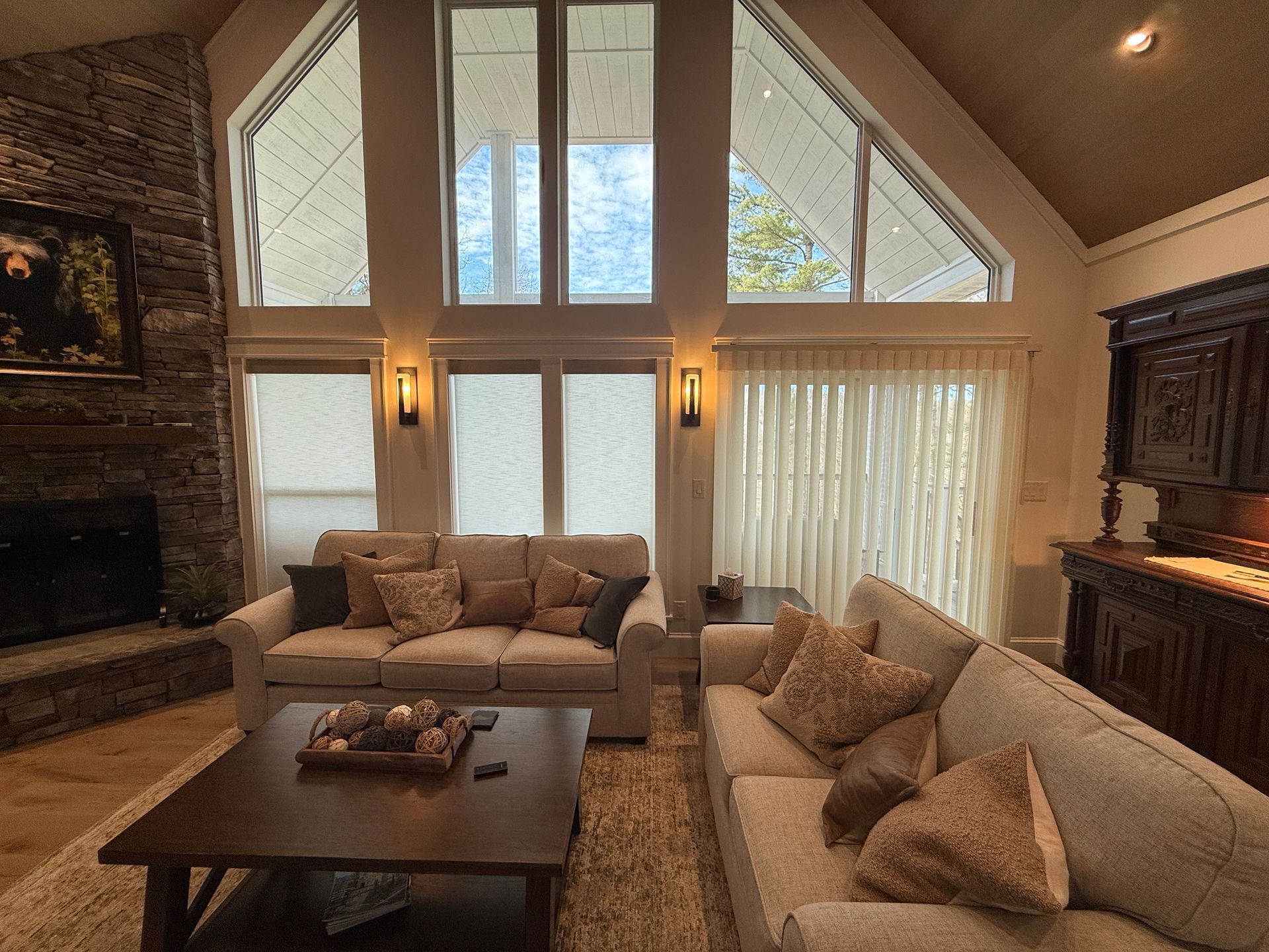 Cozy living room with beige sofas, dark wood coffee table, tall windows, and stone fireplace