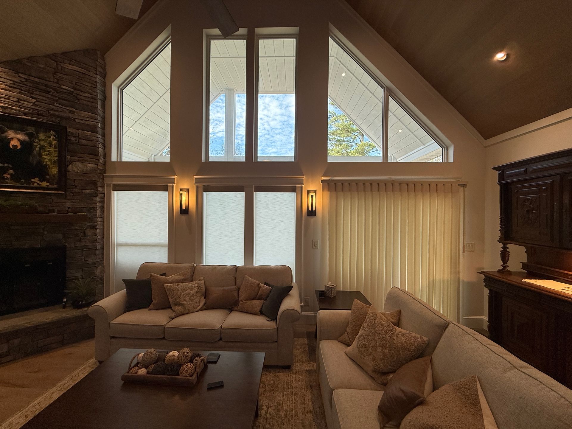 Spacious living room with vaulted ceiling, large windows, fireplace, and neutral sofas.