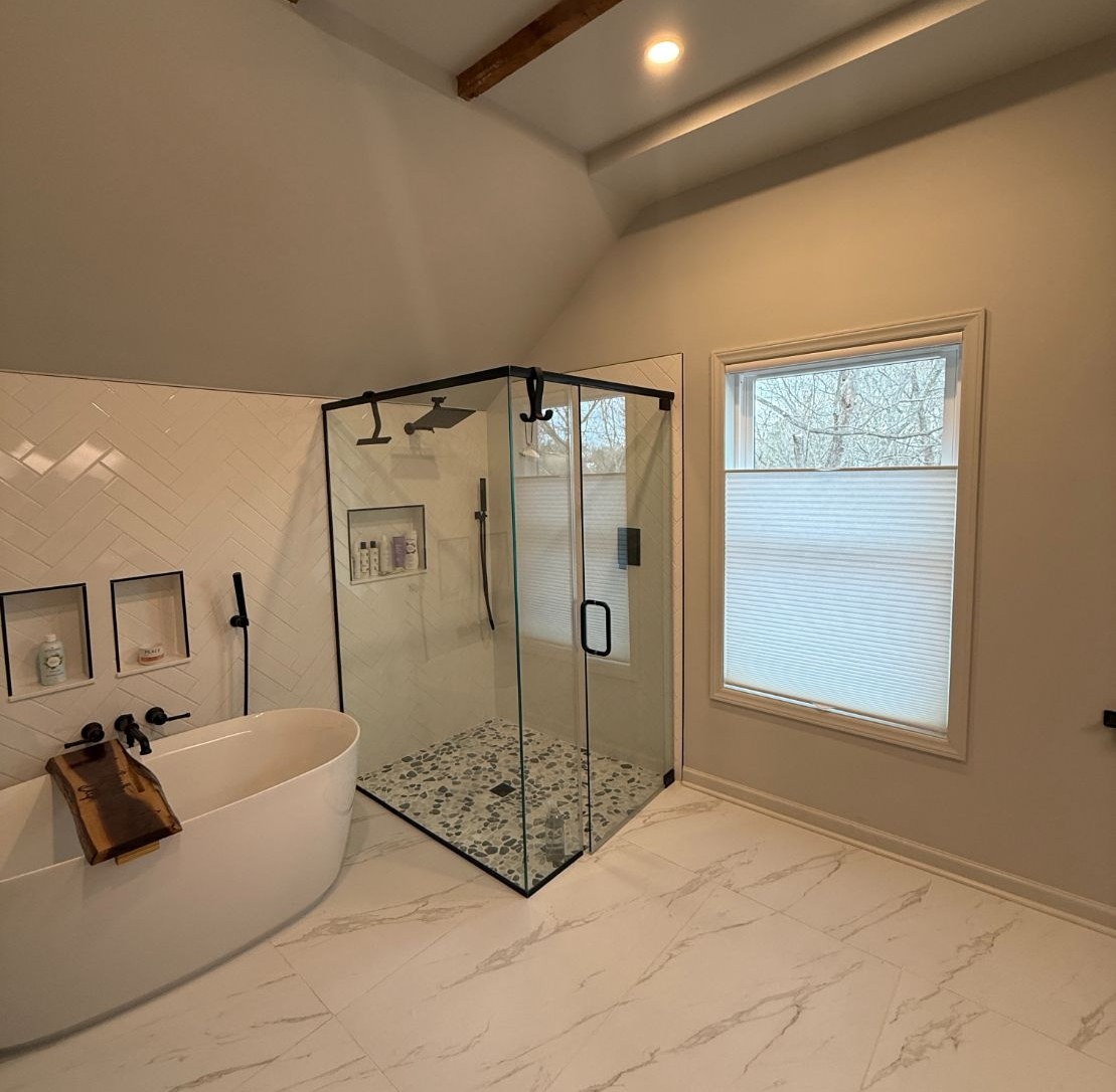 Modern bathroom with freestanding tub, glass shower, wood beams, and window cellular shades