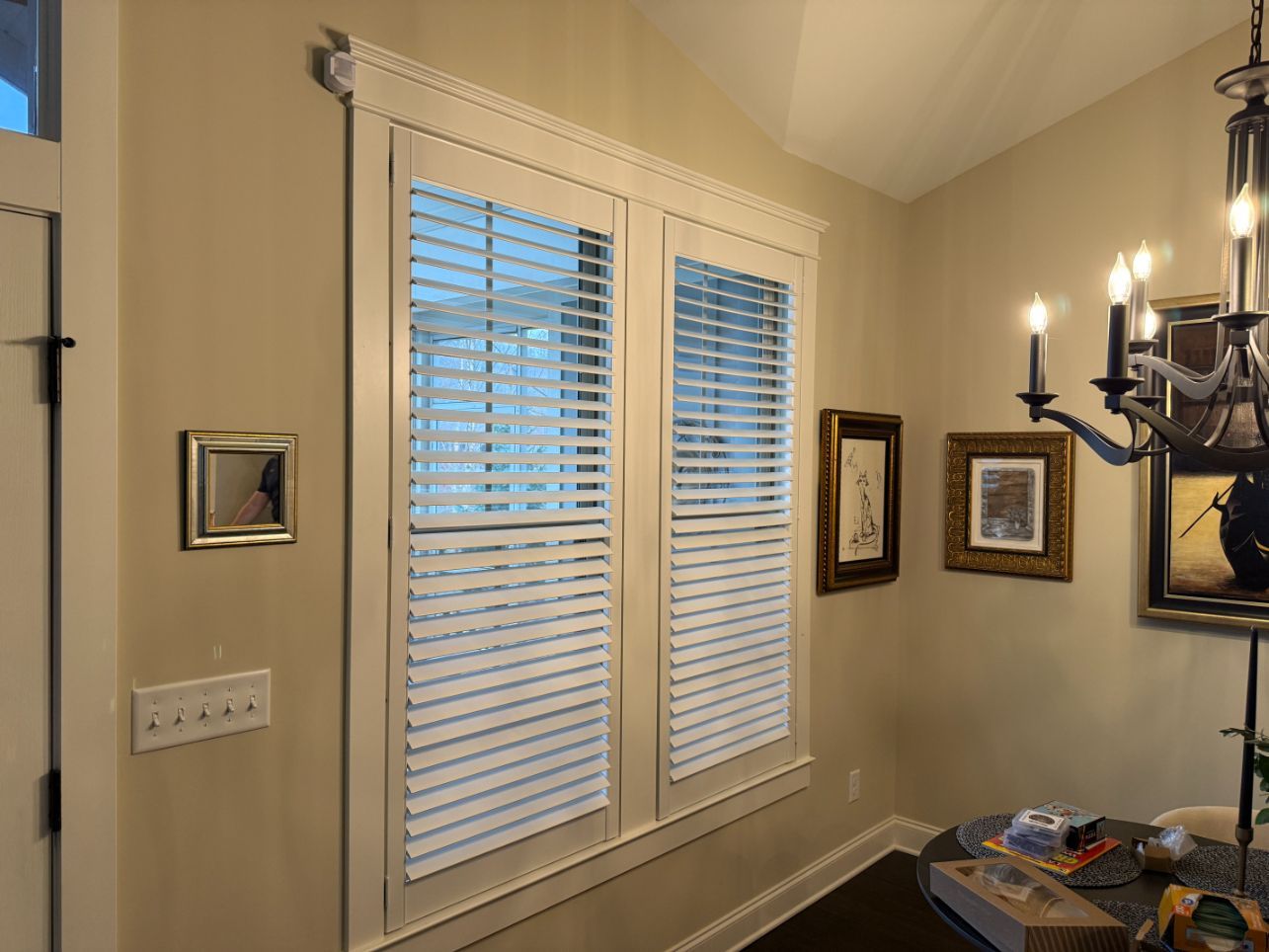 Beige hallway with white window blinds, framed wall art, and a chandelier on the right