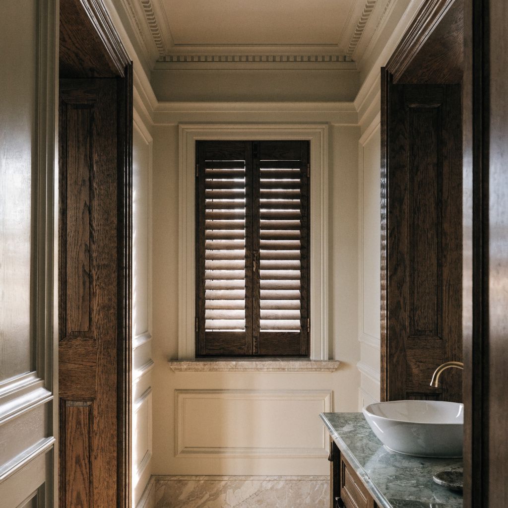 Elegant bathroom with dark wood shutters, cream walls, and a marble sink counter