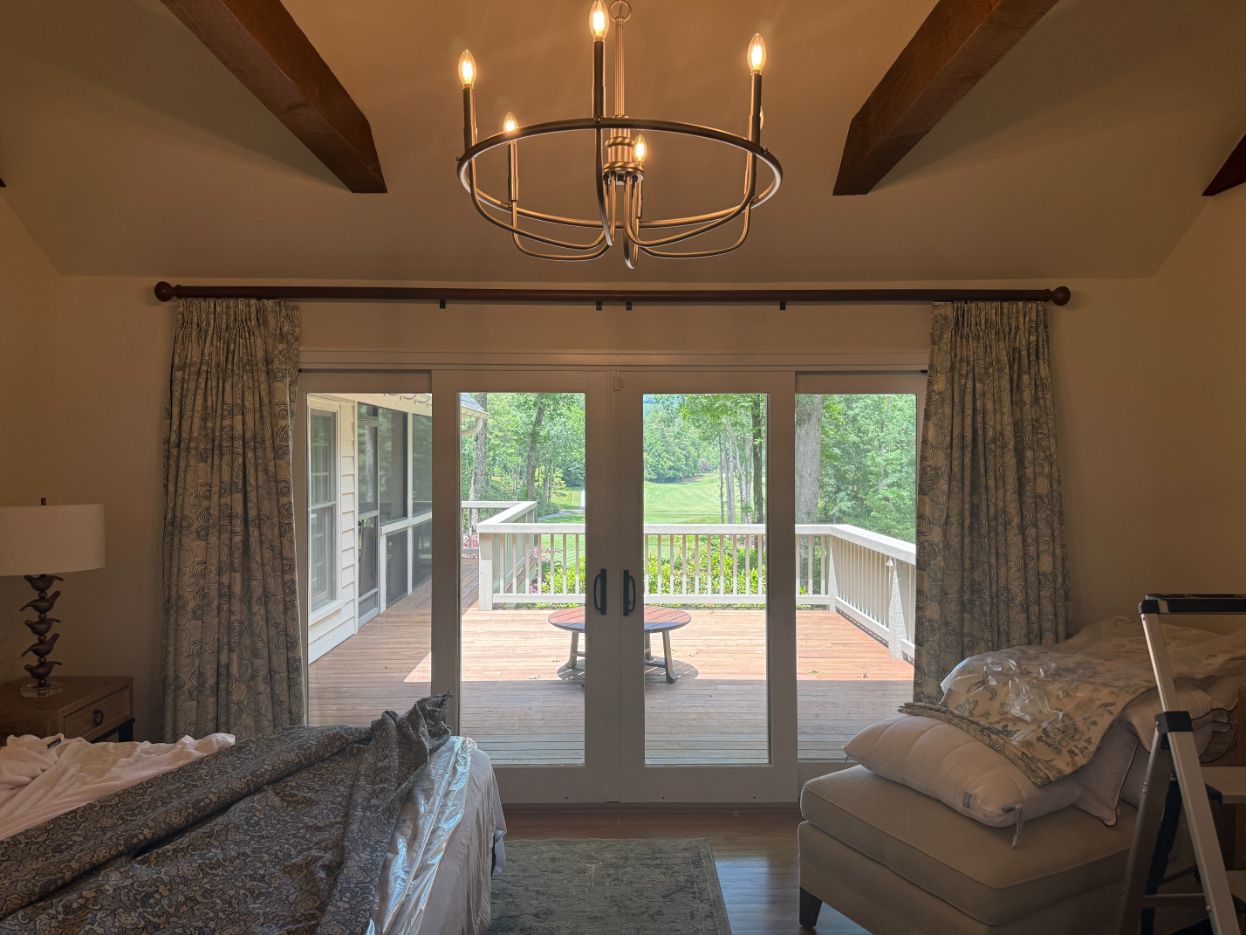 Bedroom with two beds, ceiling fan light, and glass doors with custom drapery opening to a deck and trees.