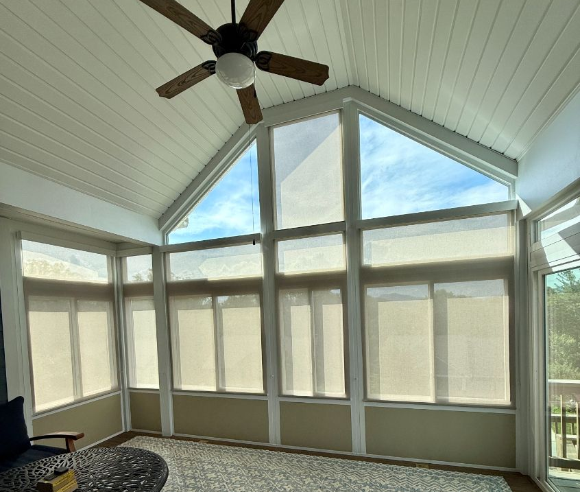 Sunroom with high windows, solar shades, ceiling fan, and patterned rug, filled with soft daylight.
