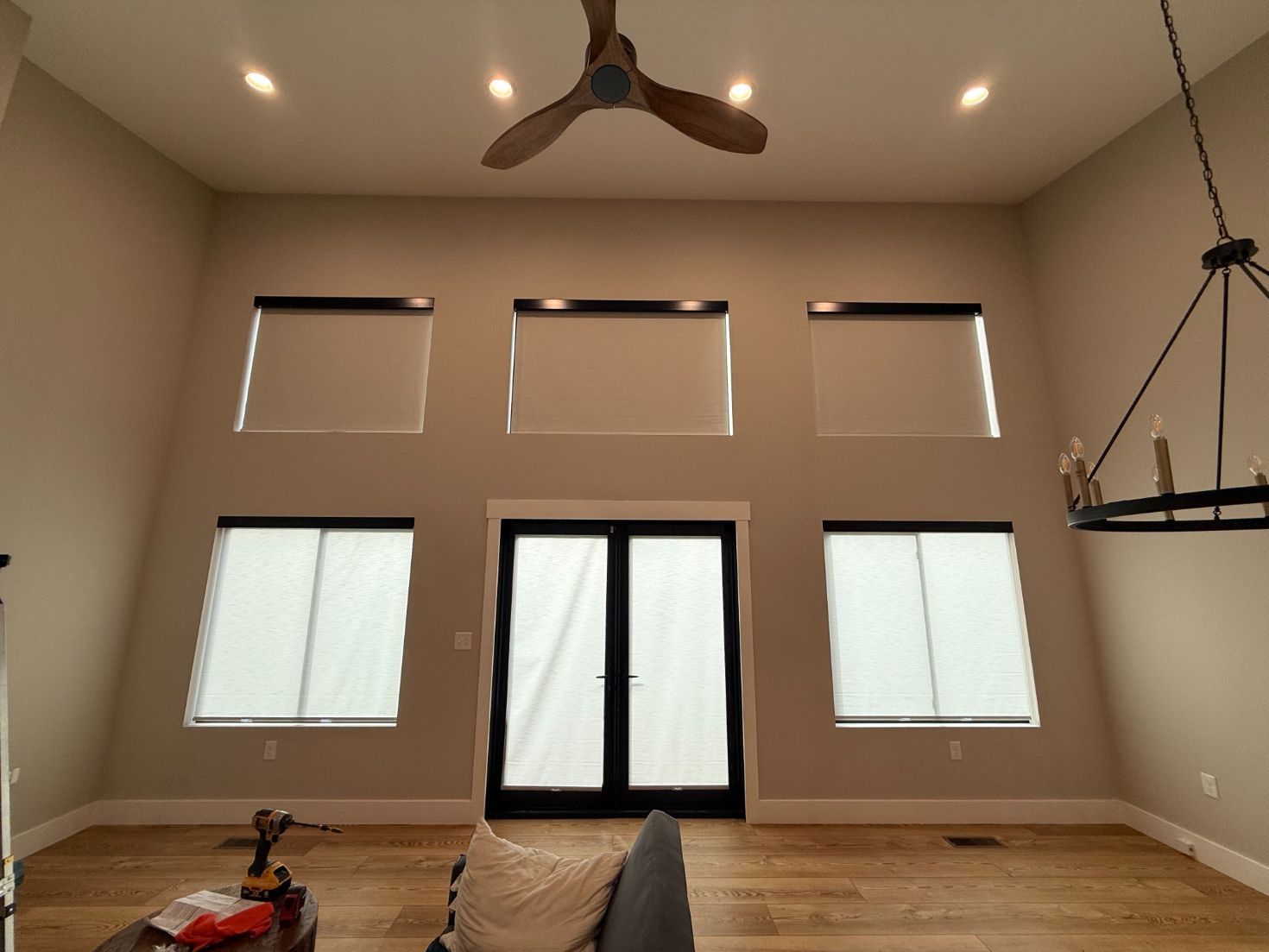 Empty modern living room with high windows, glass doors, wood floors, and ceiling fans.