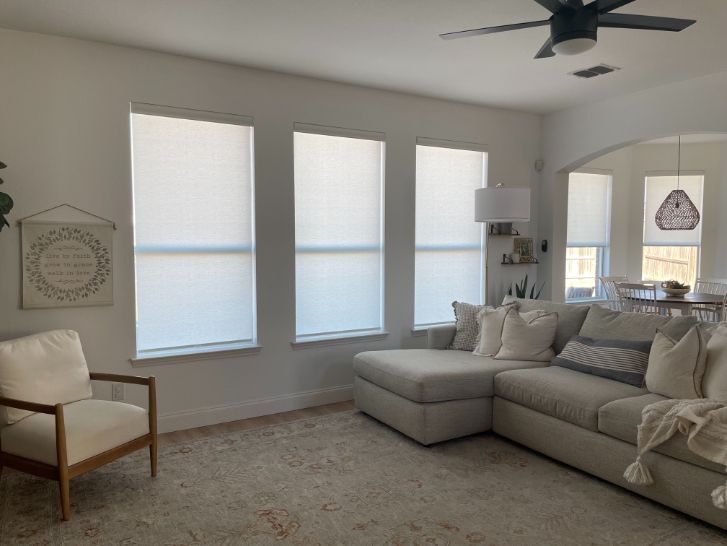 Bright living room with gray sectional, three windows, beige chair, and ceiling fan