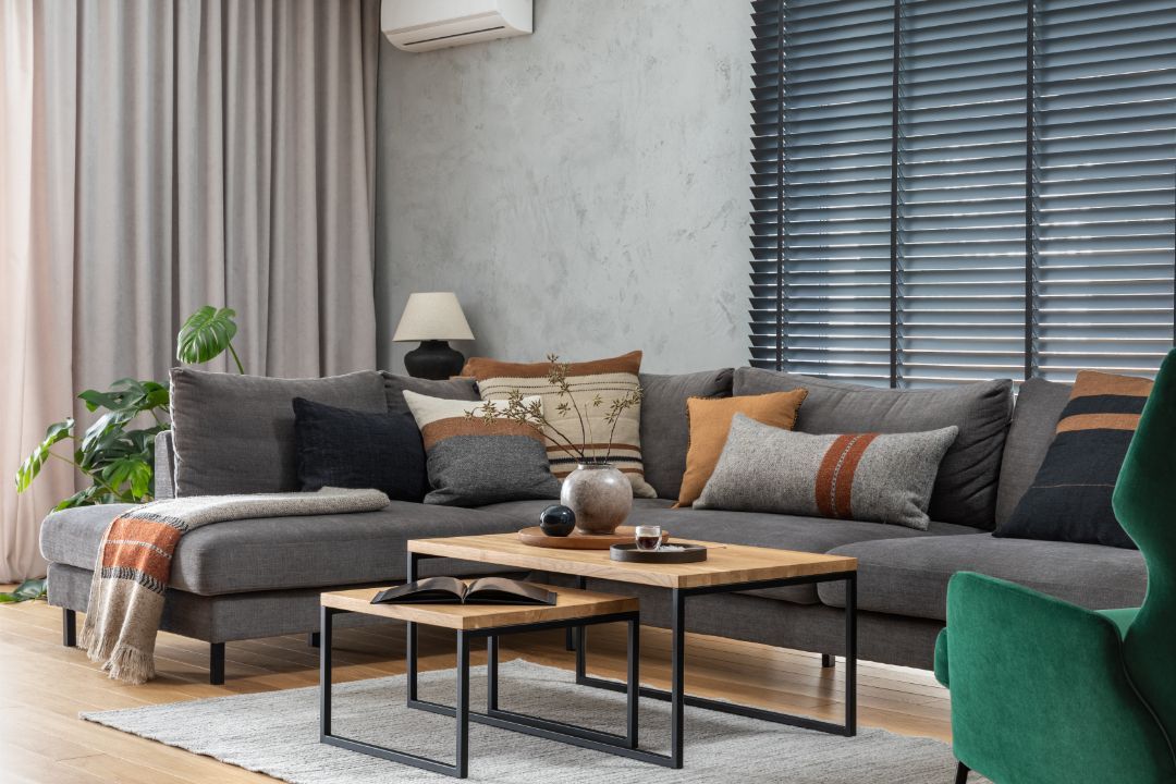 Modern living room with gray sofa, green chair, coffee tables, and large windows with blinds