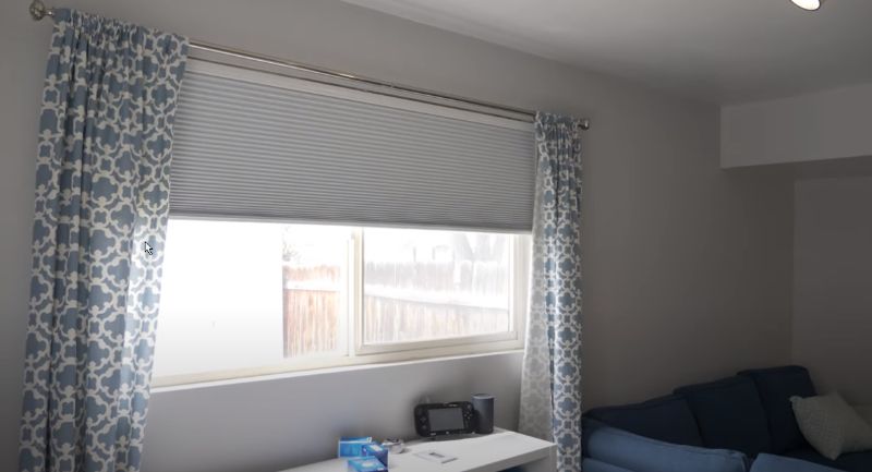 Bright living room window with blue patterned curtains, white blinds, and a couch on the right.