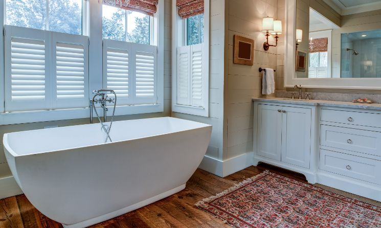 Bright bathroom with freestanding tub, double vanity, and large windows with shutters