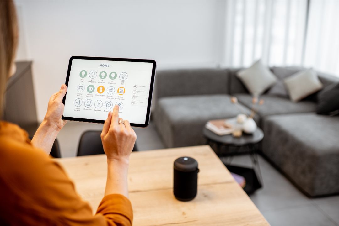 Person using a tablet in a cozy living room with a gray sofa and a black smart speaker on the table