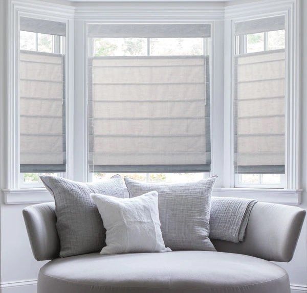Gray sofa with white and gray pillows in front of bright bay windows with blinds
