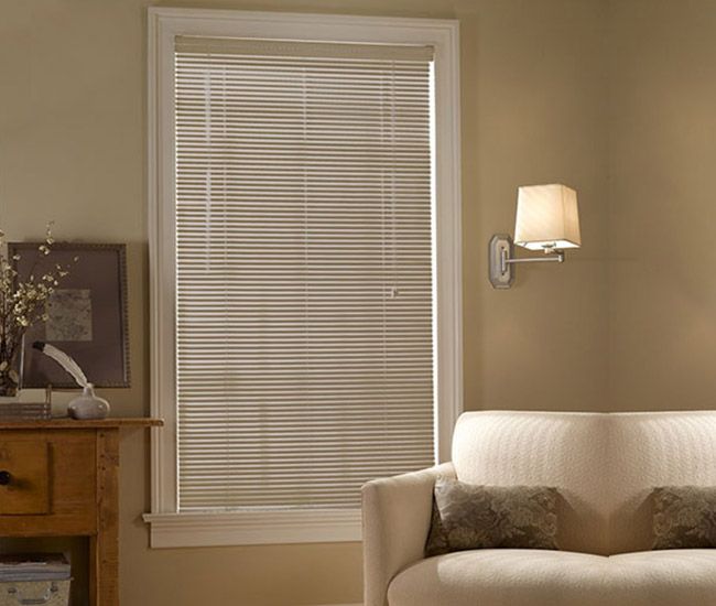 Cozy living room with beige sofa, wall lamp, window blinds, and wooden dresser