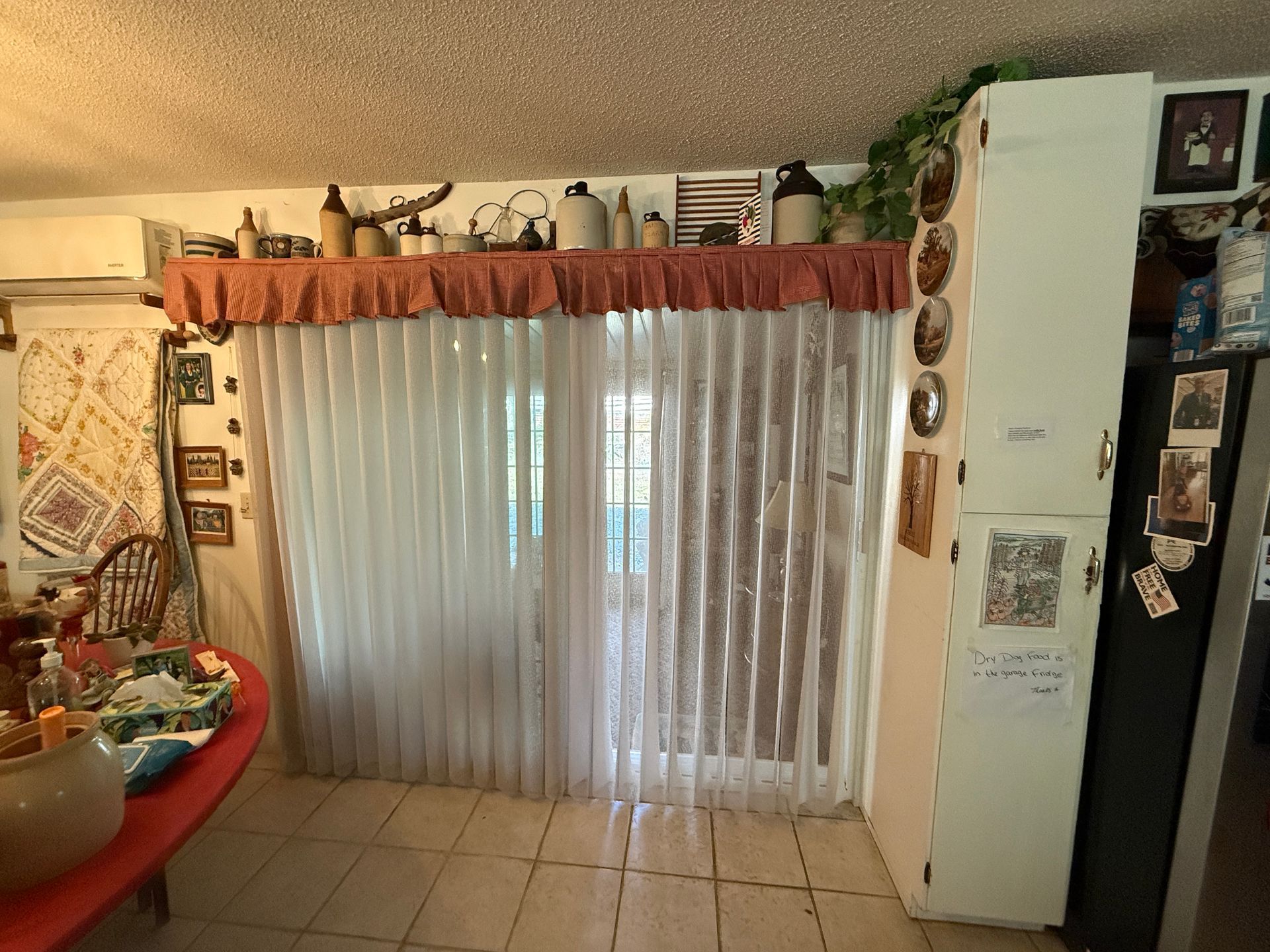 A kitchen with a sliding glass door covered by white vertical blinds and a decorative valance.