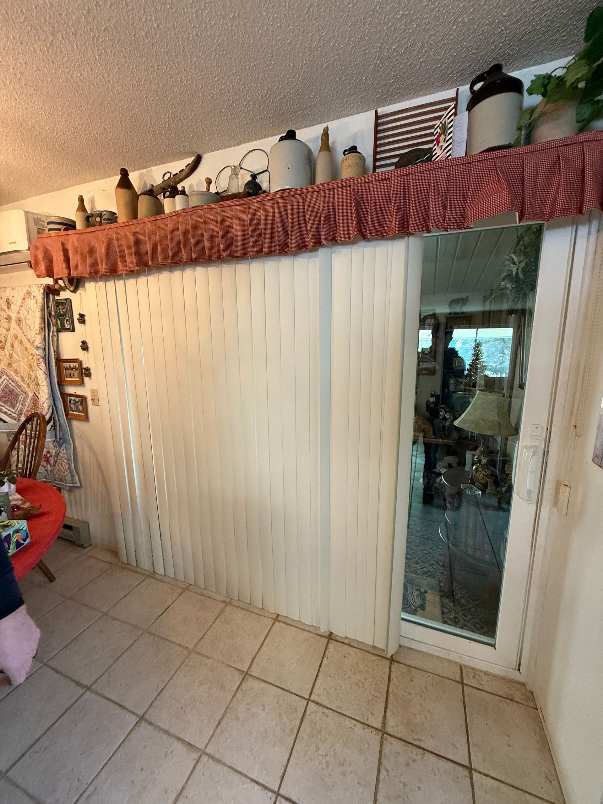 Vertical blinds and sliding glass door with a decorative valance, displaying items on a shelf above.