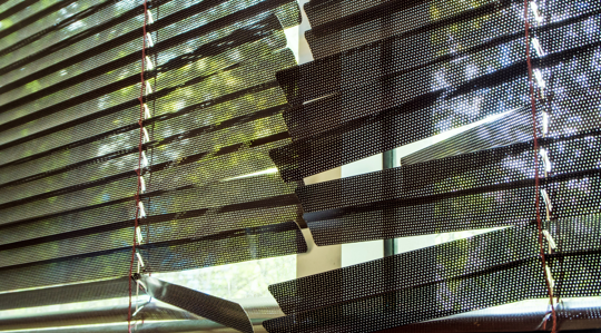 Sunlight through window blinds casting striped shadows on a screened outdoor patio