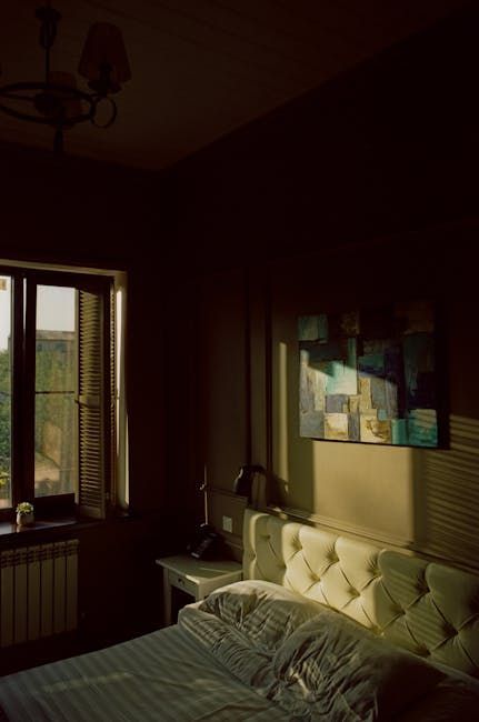 Sunlit bedroom with an open window, tufted bed, and abstract wall art in warm shadows