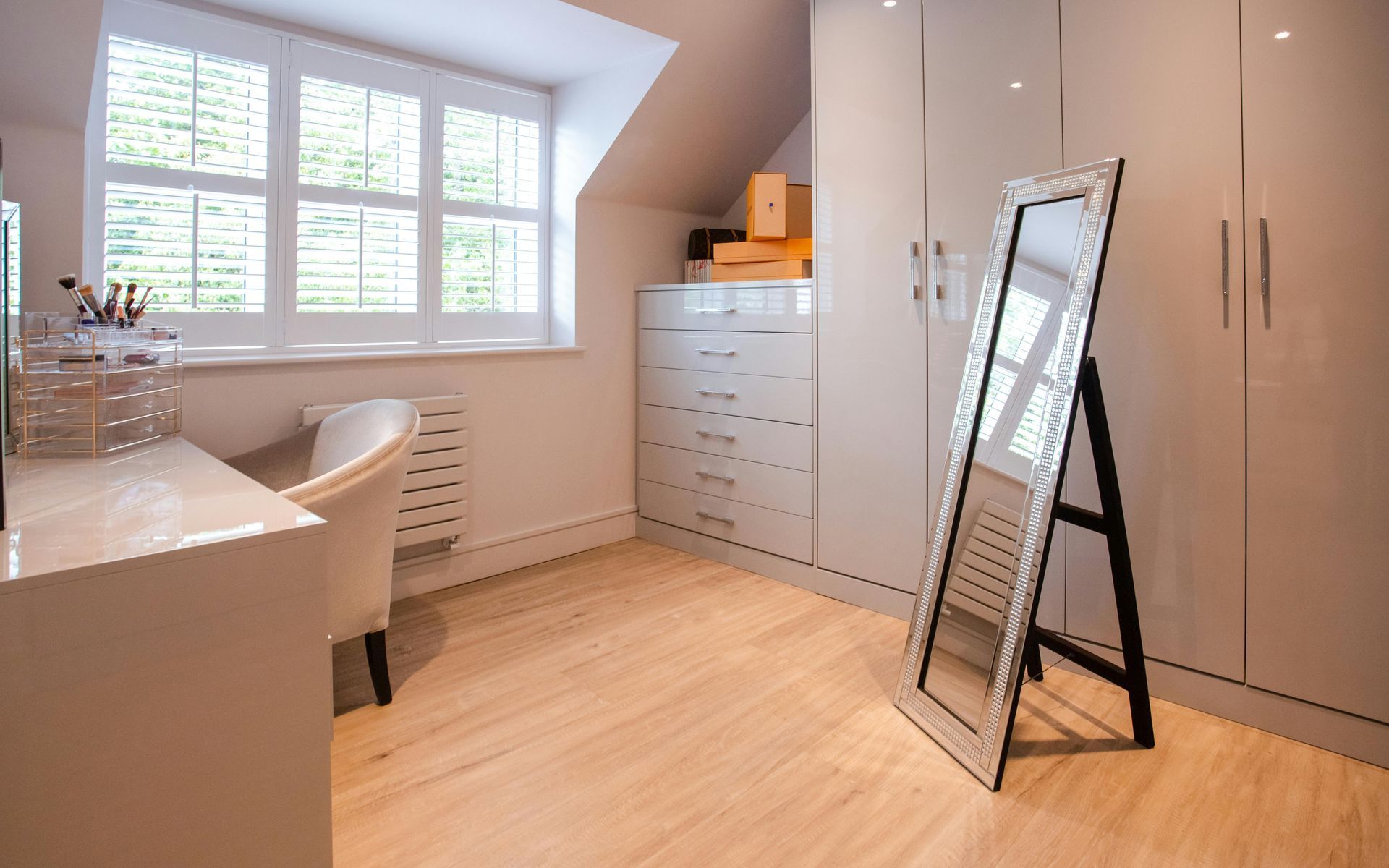 Bright bedroom with white built-in wardrobes, window seating, and a large leaning mirror on the floor.