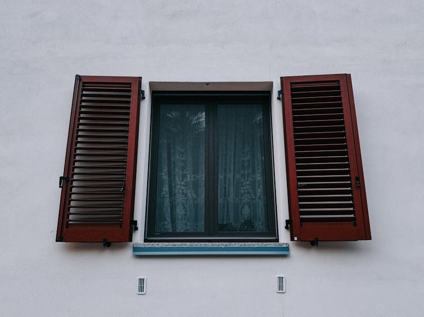 Closed window with dark shutters on a white wall