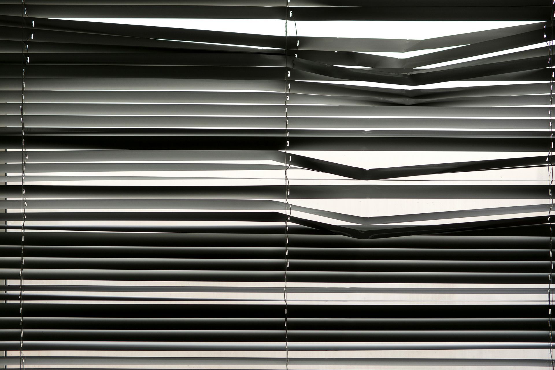 Closed window blinds with a few bent slats, creating horizontal black-and-white stripes.