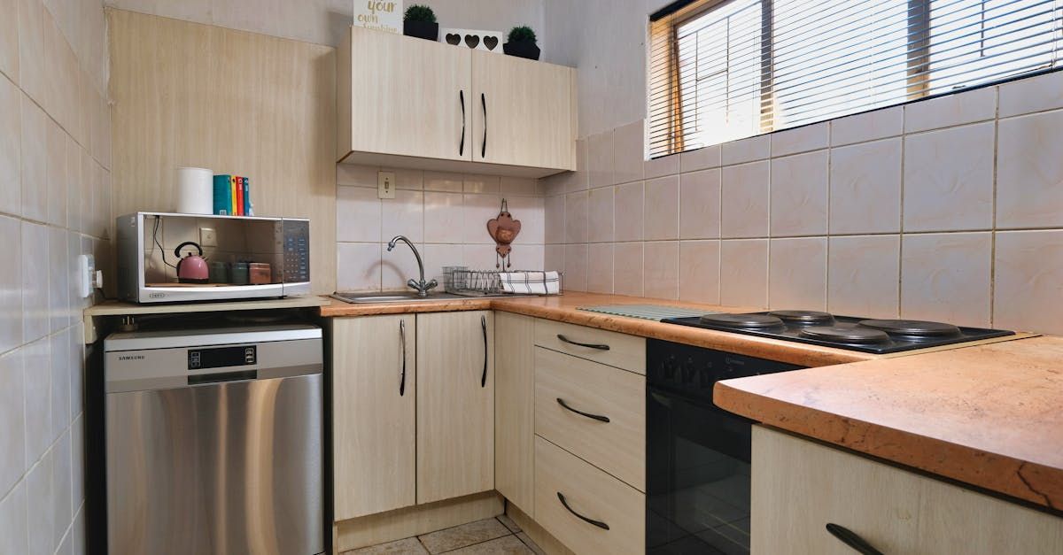 Small kitchen with beige cabinets, tiled backsplash, wood counters, sink, stove, and stainless-steel dishwasher.