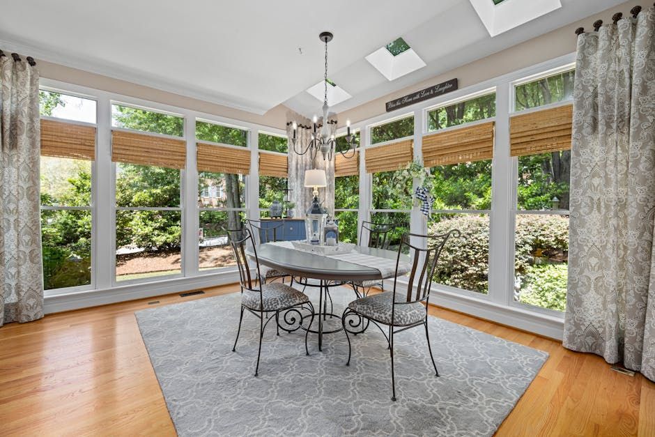 Bright sunroom with round dining table, metal chairs, skylights, and garden views through large windows