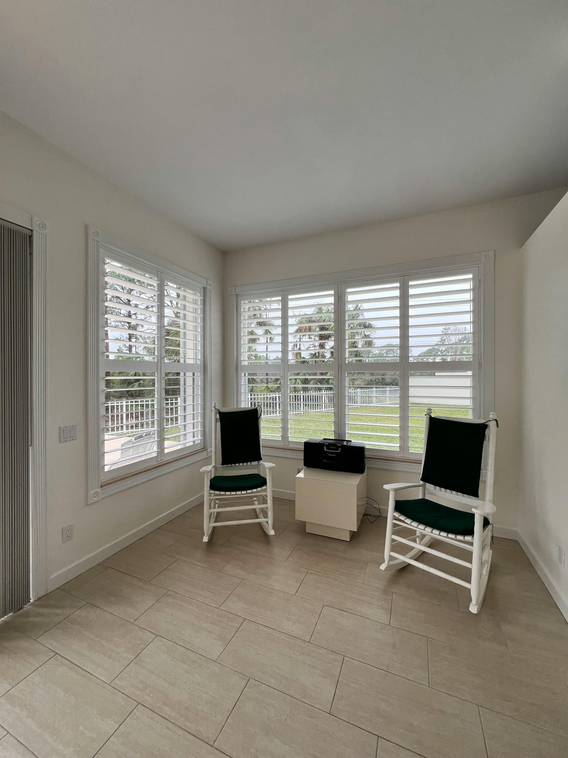 Bright corner room with large windows, white tile floor, and three black-and-white chairs around a small table.