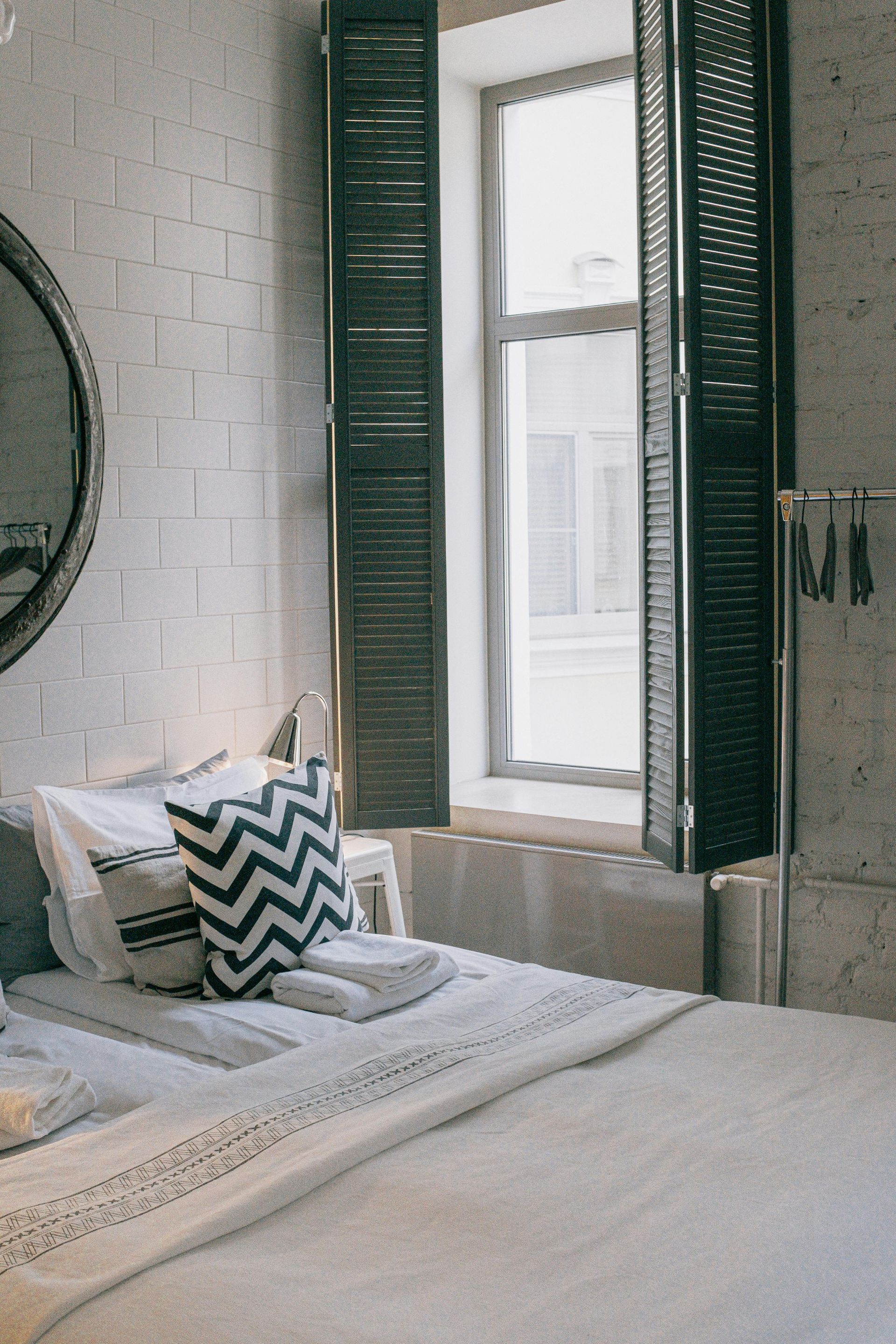 Bright bedroom with white bedding, chevron pillows, and green shutters beside a sunlit window