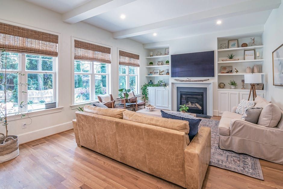 Bright living room with beige sofa, fireplace, wood floors, and large windows with woven shades