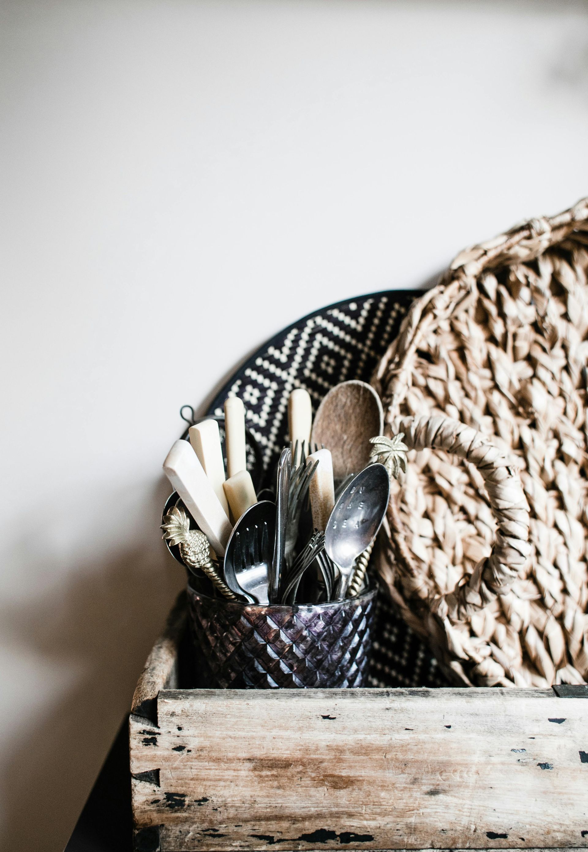 Wooden utensil holder with spoons and forks beside a woven basket on a textured surface