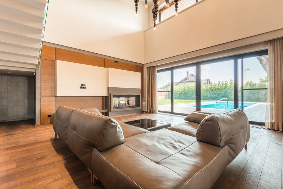 Modern living room with tan sectional, fireplace, and large glass doors opening to a pool and backyard.