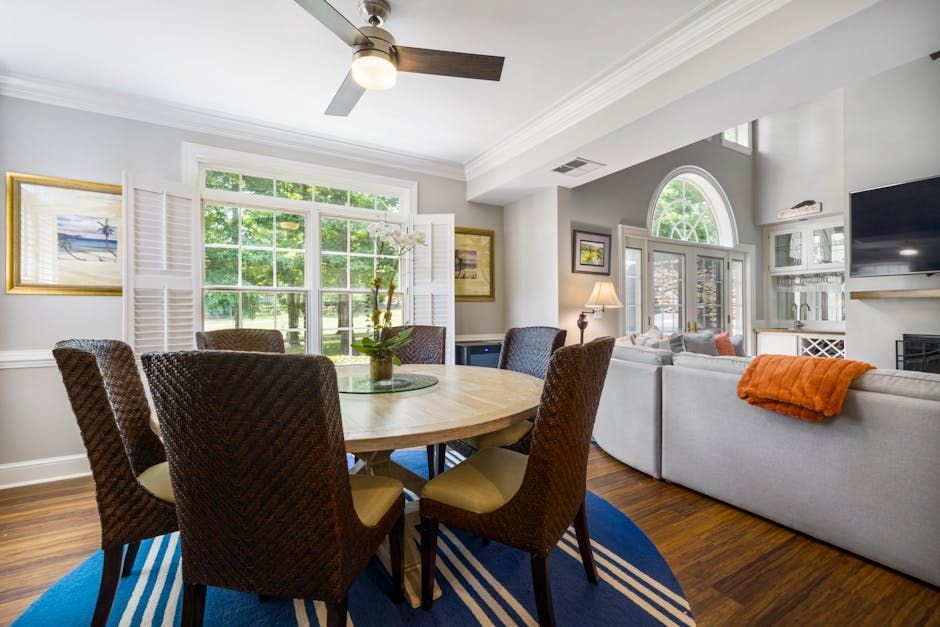 Bright dining room with round table, woven chairs, sofa, and large windows.
