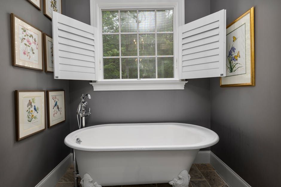 Bright bathroom with a white clawfoot tub, window, and open shutters on gray walls.