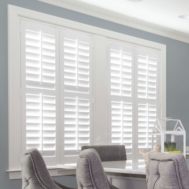 Bright dining area with large white shutters, gray walls, and gray chairs by a window