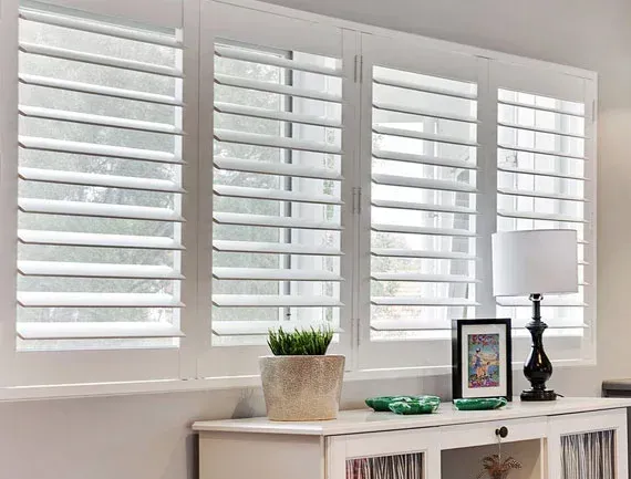 Bright room with white plantation shutters above a cabinet holding a plant, lamp, and framed art