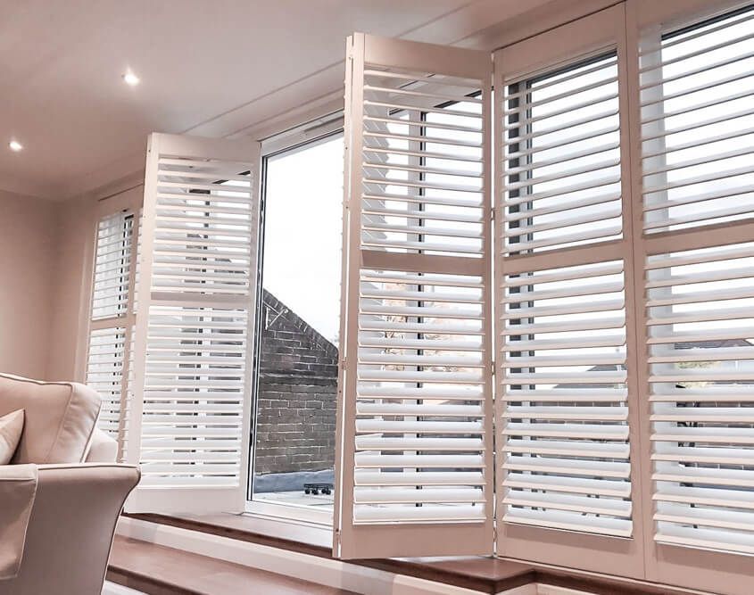 Bright living room with white plantation shutters and a view of the outdoors through an open window