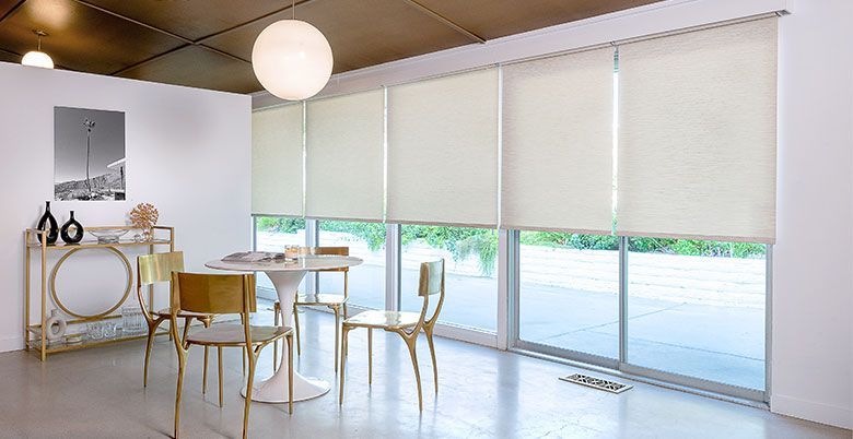 Bright modern dining room with gold chairs, round table, and large window blinds overlooking a patio.