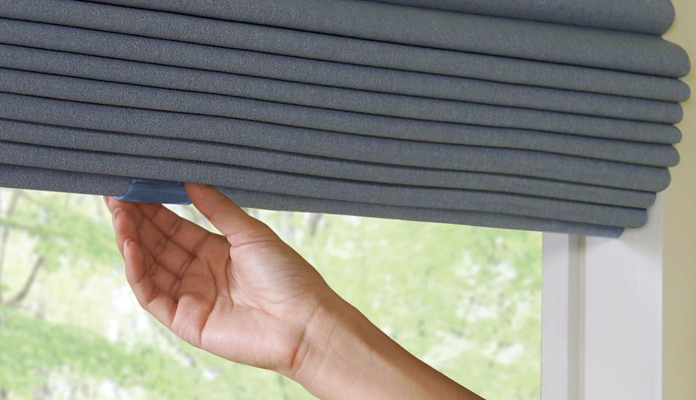 Hand adjusting a gray window blind by a bright window