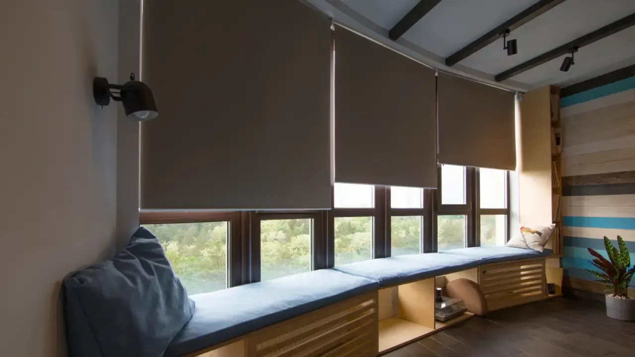 Modern room with a blue window seat, roller blinds, and a built-in wooden desk by the windows.